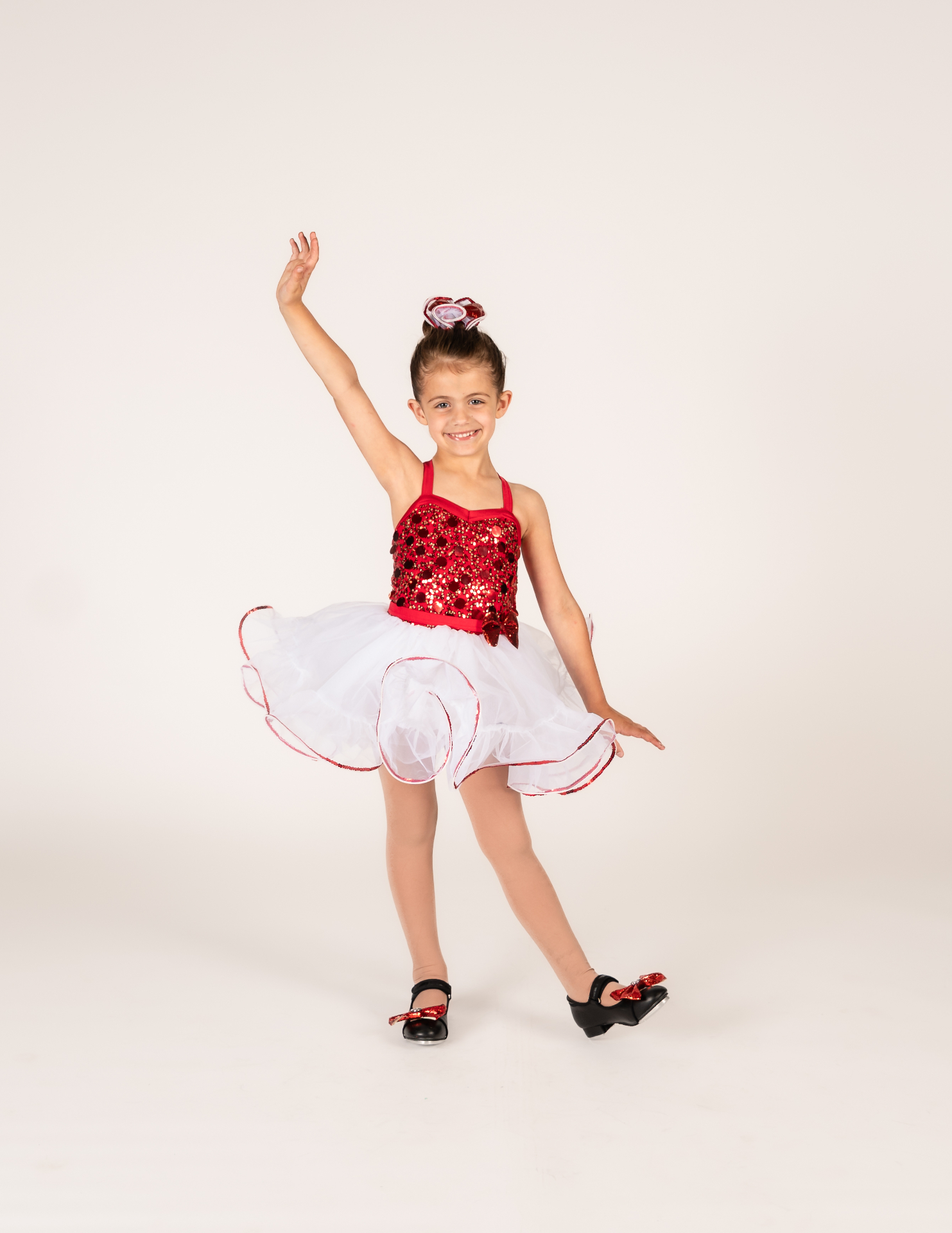 Young dancer in a red sequin top and white tutu posing in tap shoes