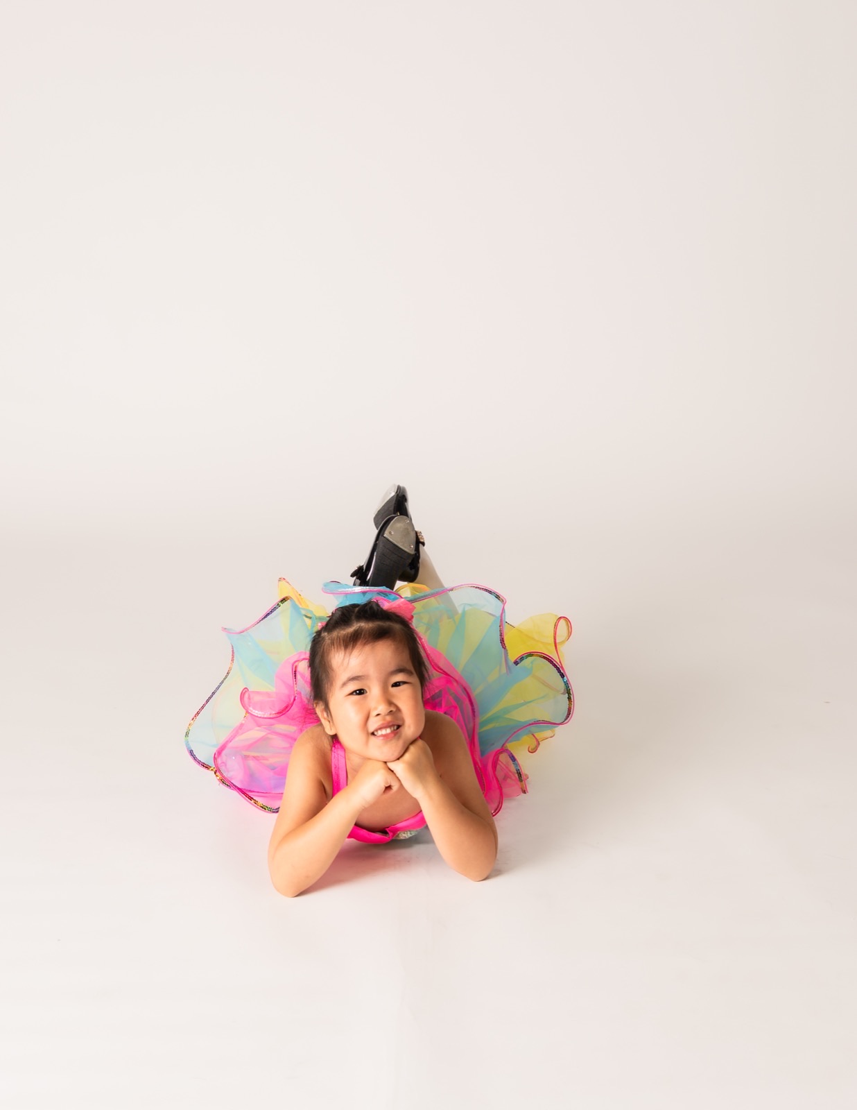 Two and three year old dancer lying on the floor in a rainbow tutu
