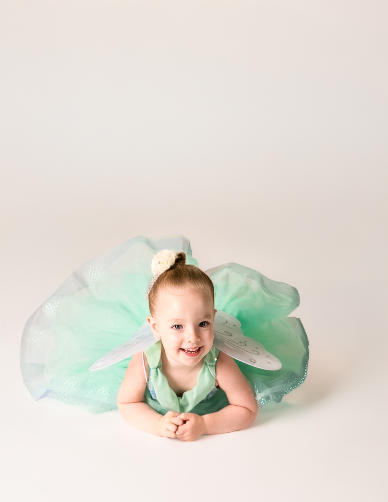 Two and three year old dancer in a mint fairy costume lying on the studio floor
