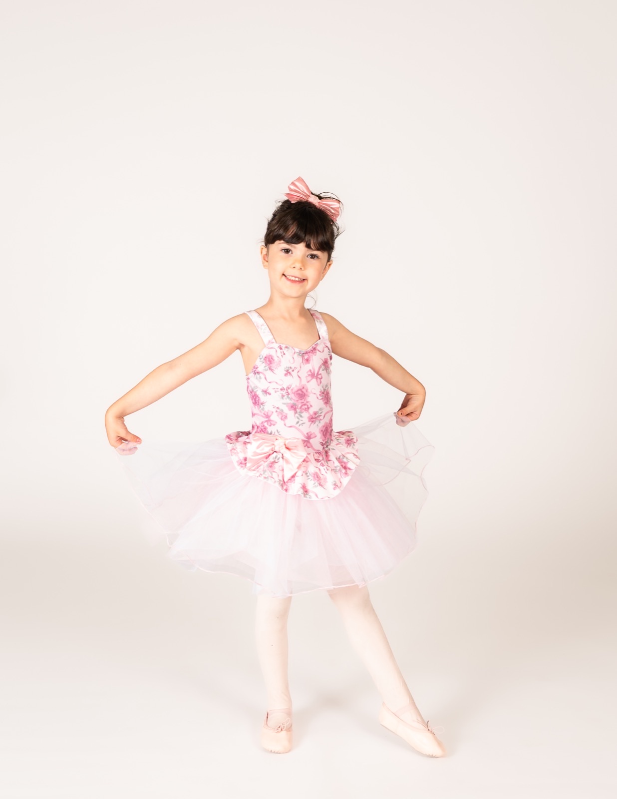 Four and five year old dancer holding out a pink floral tutu